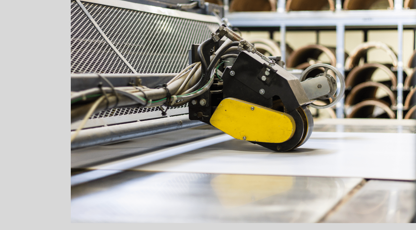 A cutting head travelling across a laminated sheet, with roll stock racked behind the line