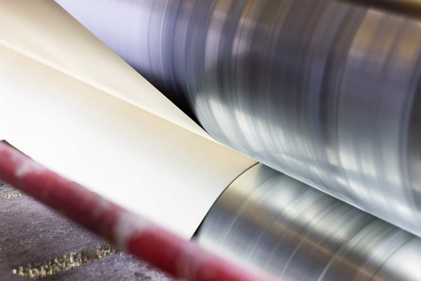 Close view of the nip point where a paper web meets the chrome roller on the laminating line